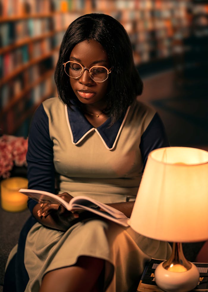 Woman reading a book in a cozy library setting with warm lighting.