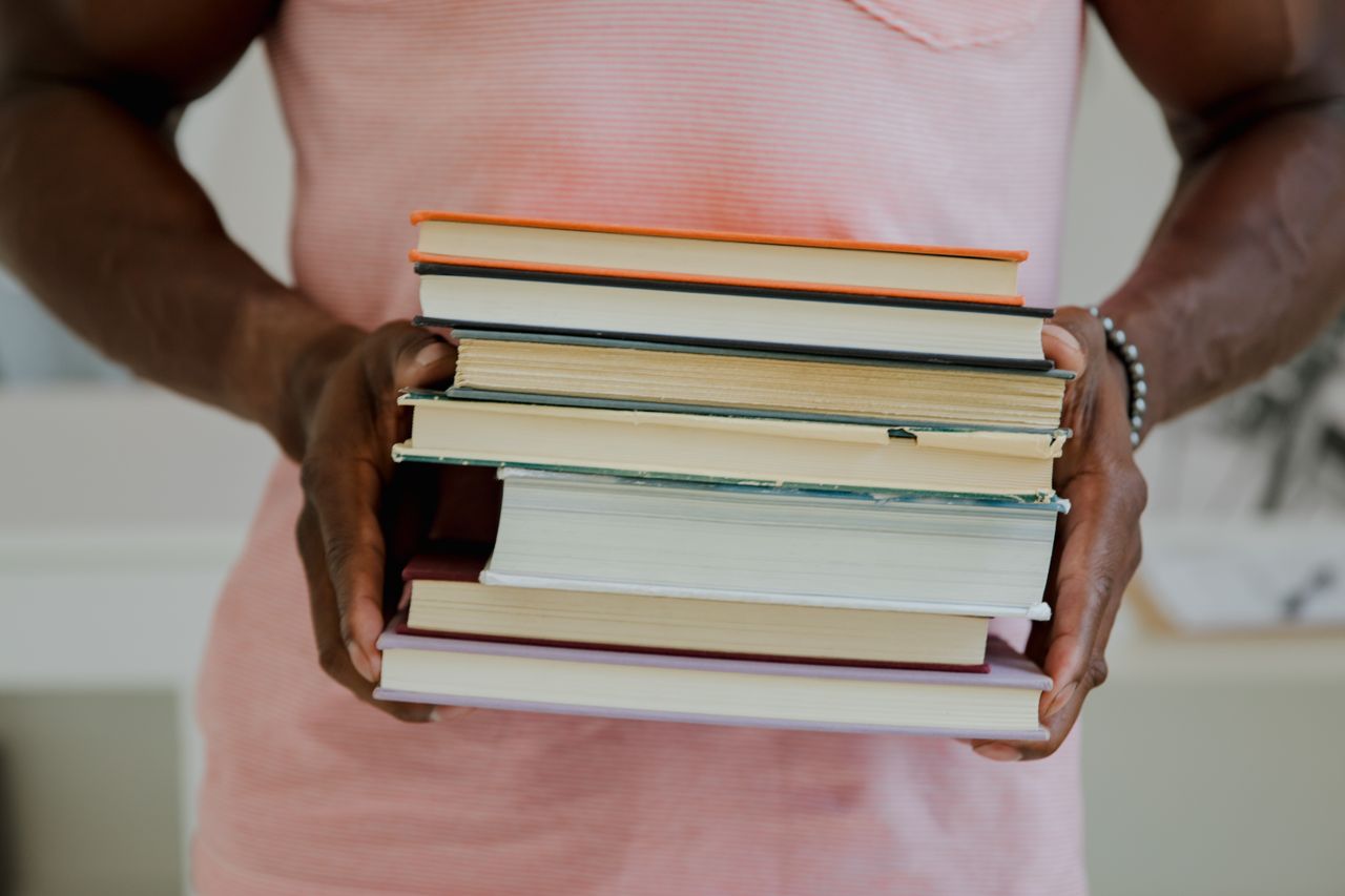 A person holding a stack of seven books indoors. Perfect for educational themes.